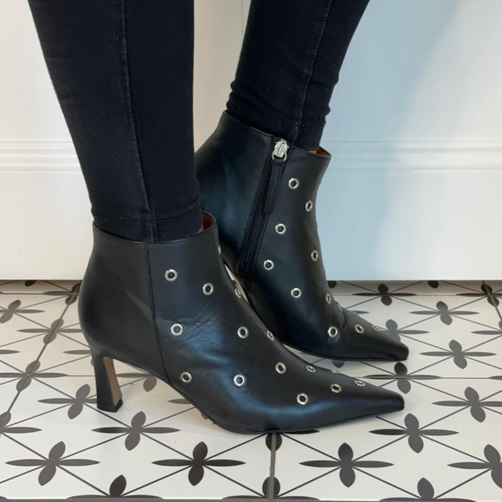 Black stiletto boots with decorative studs worn indoors on a patterned floor. Ángel Alarcón Clarine 25558 Leather Ankle Boot-BLACK