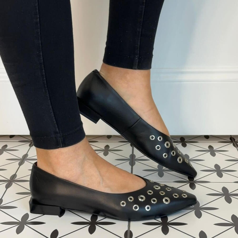 Black studded flats worn with black pants on a patterned floor. Ángel Alarcón Sila 25509 Flat Leather shoe-BLACK