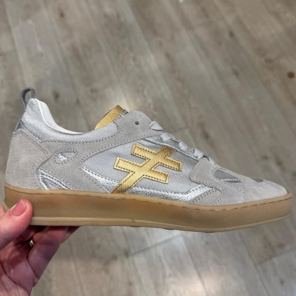Another Trend Gray sneaker with gold logo held by a hand on a wooden floor.