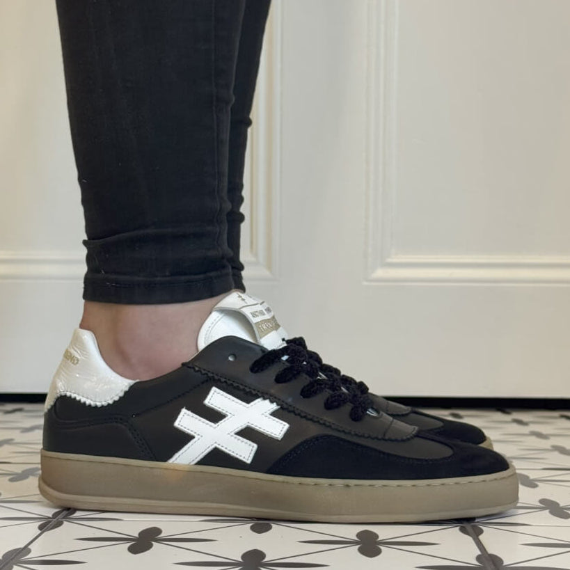 Black sneakers with white accents worn indoors on a patterned floor. Another Trend Iconic Leather Sneakers A032-Black & White