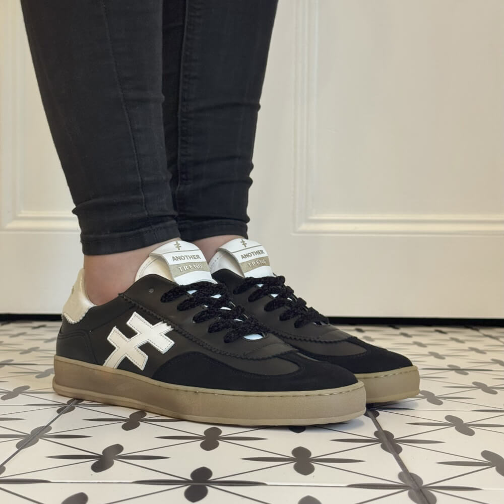 Black sneakers with white accents worn indoors on a patterned floor. Another Trend Iconic Leather Sneakers A032-Black & White