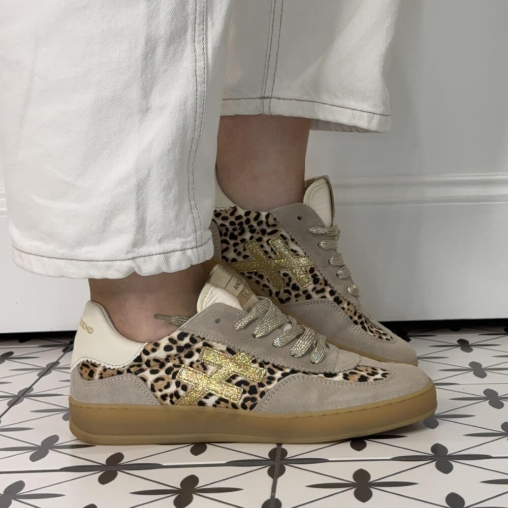 Another Trend Beige sneakers with leopard print and gold accents worn with white pants on a patterned floor.