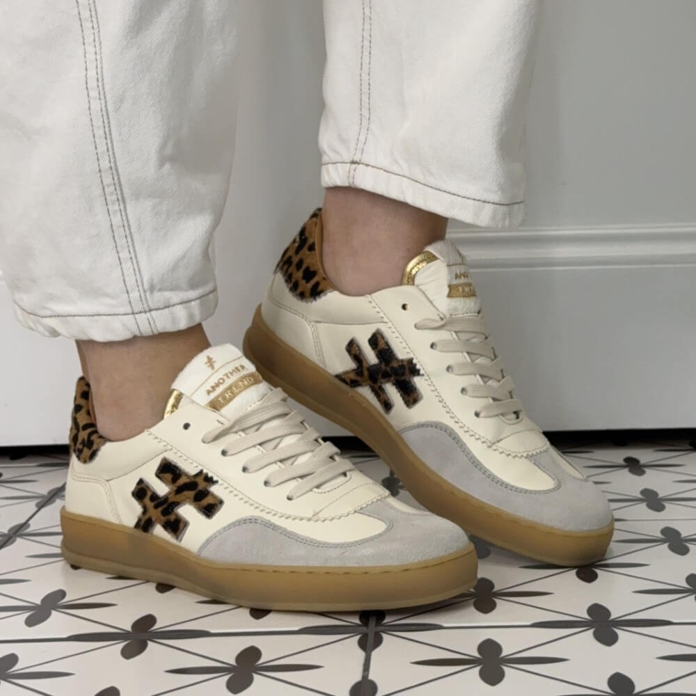 White sneakers with brown soles and leopard print accents worn by a person on a patterned floor.