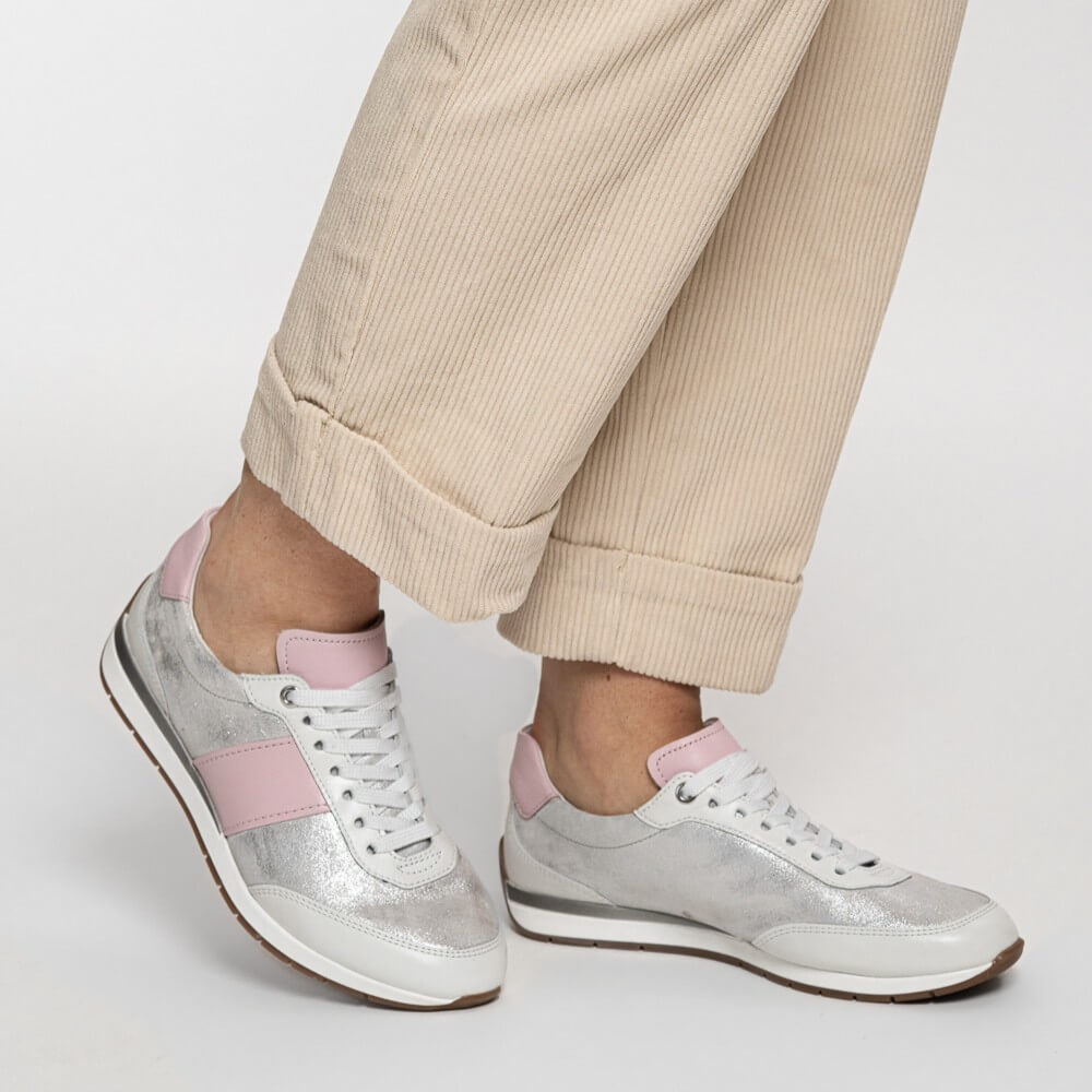 Person wearing silver sneakers with pink accents and beige pants on a light gray background