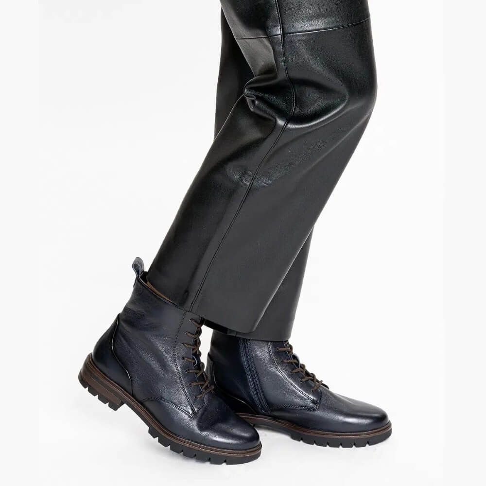 A close-up of a person's legs wearing black leather trousers and Ara dark navy blue leather lace-up boots with brown soles, set against a plain white background.