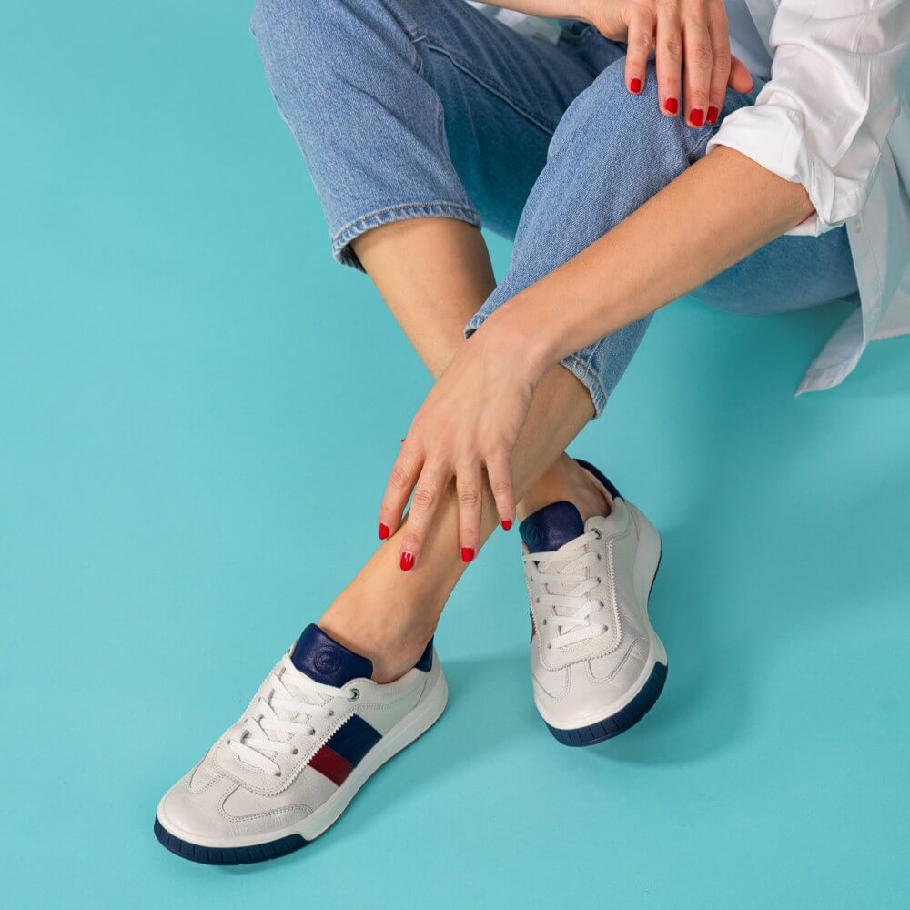 Person wearing white sneakers with blue accents on a teal background