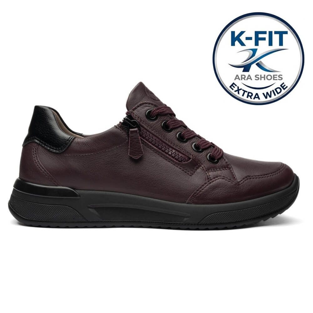 Ara dark burgundy leather low-top shoe with a black sole, on a white background. A circular blue and white 'K-FIT ARA SHOES EXTRA WIDE' logo badge is positioned in the top right corner.