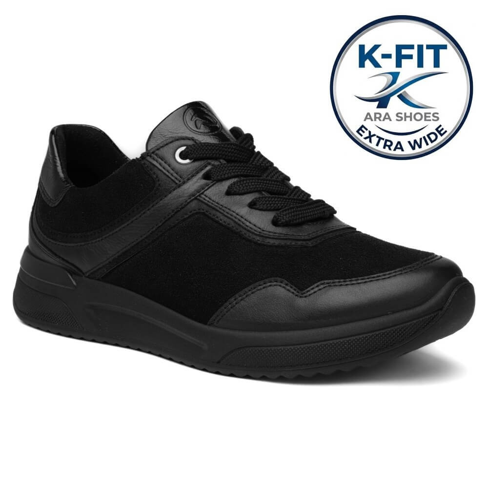 A black low-top sneaker shown from a three-quarters angle on a white background, featuring a circular 'K-FIT ARA SHOES EXTRA WIDE' badge in the top right corner.