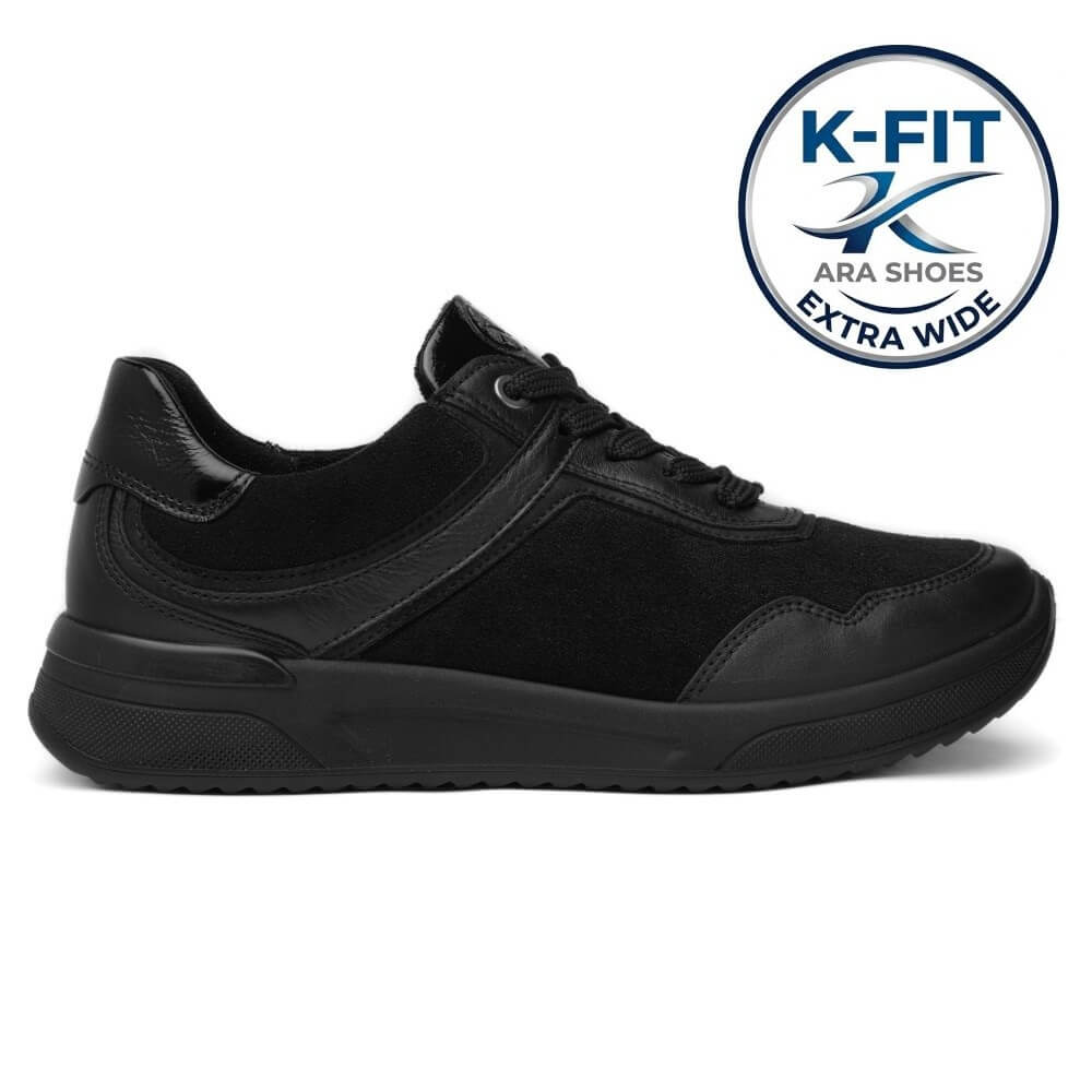 A black wide-width sneaker shown from a side profile view on a white background, featuring a circular 'K-FIT ARA SHOES EXTRA WIDE' badge in the top right corner.