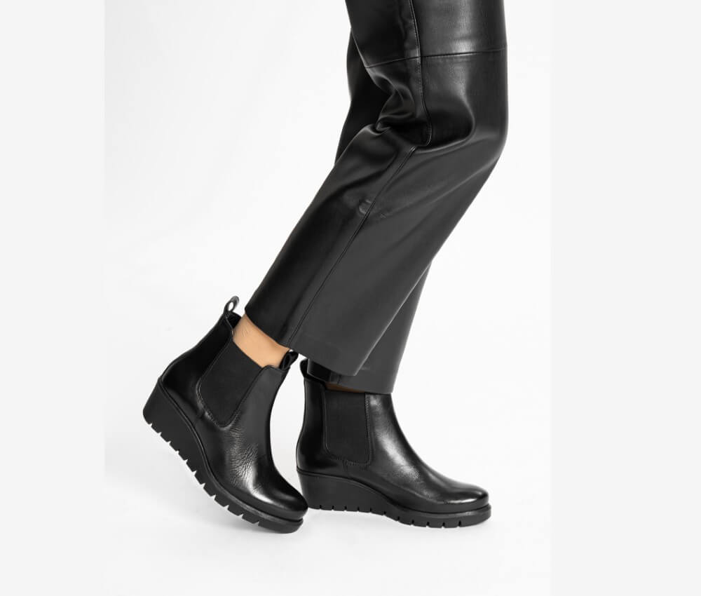 Black Leather Wedge boots worn with black pants on a white background