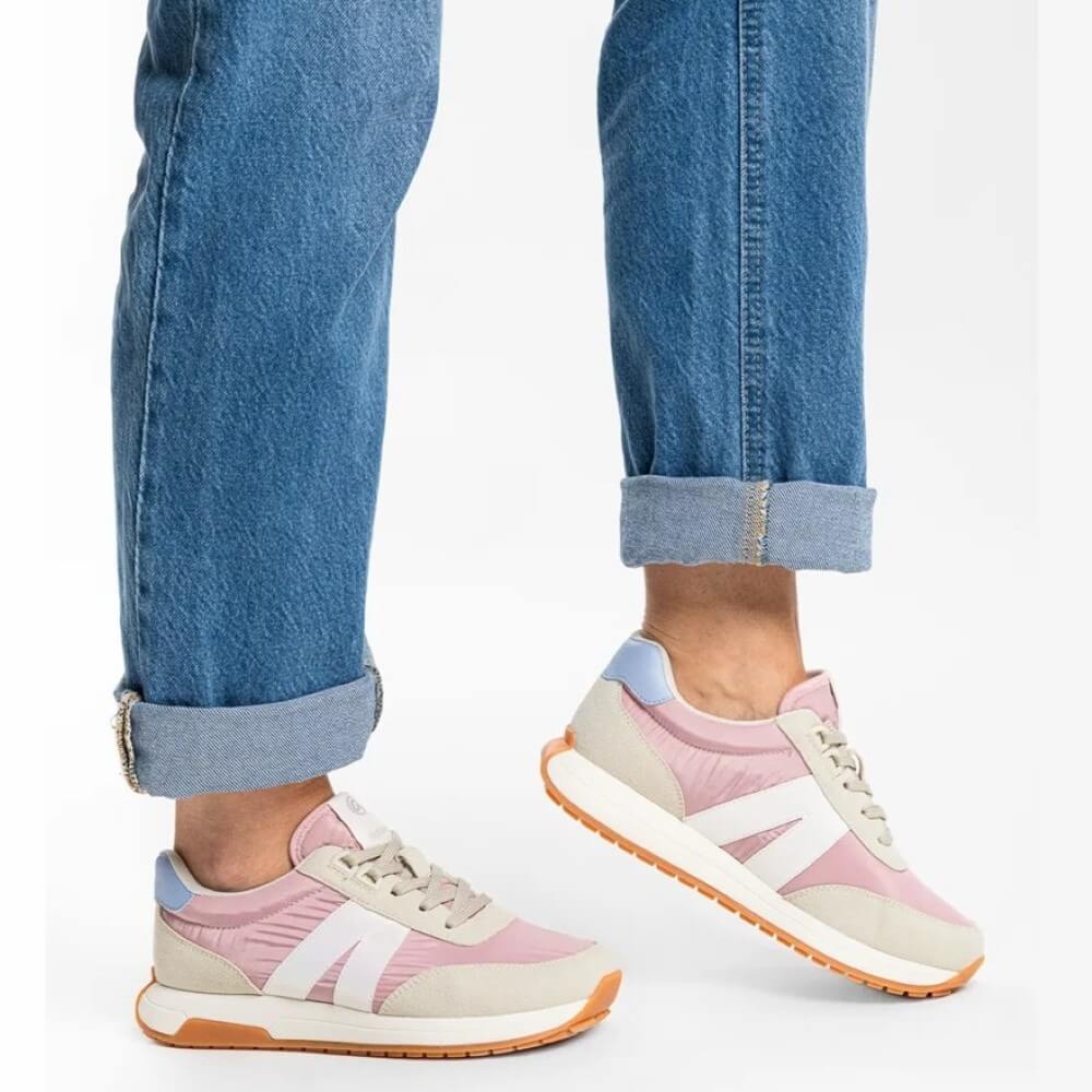 Pastel pink and beige sneakers worn with rolled-up blue jeans on a white background