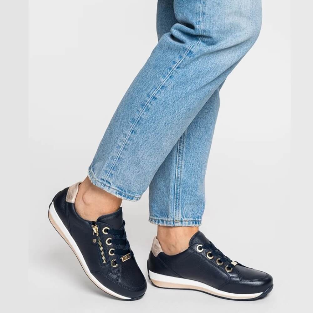 Navy sneakers with white soles worn with light blue jeans on a light gray background