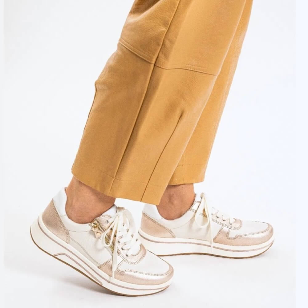 Beige and White sneakers worn with mustard yellow pants on a white background