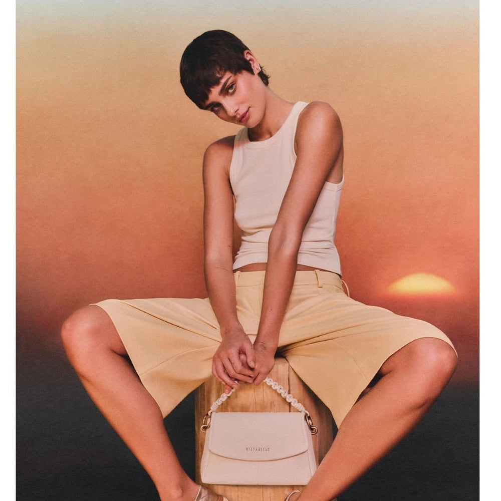 Woman sitting with a beige handbag against an orange gradient background