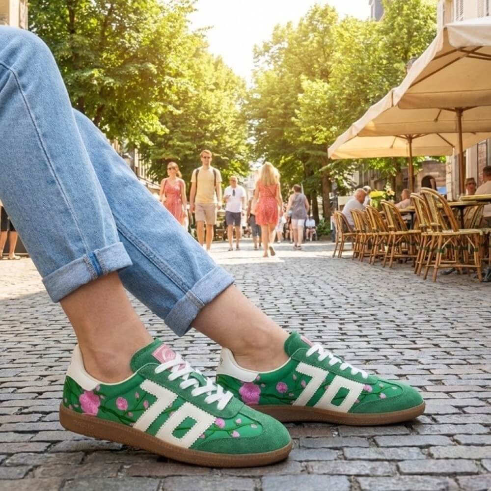 Back 70 Green sneakers with floral patterns worn on a street with people and outdoor seating in the background.