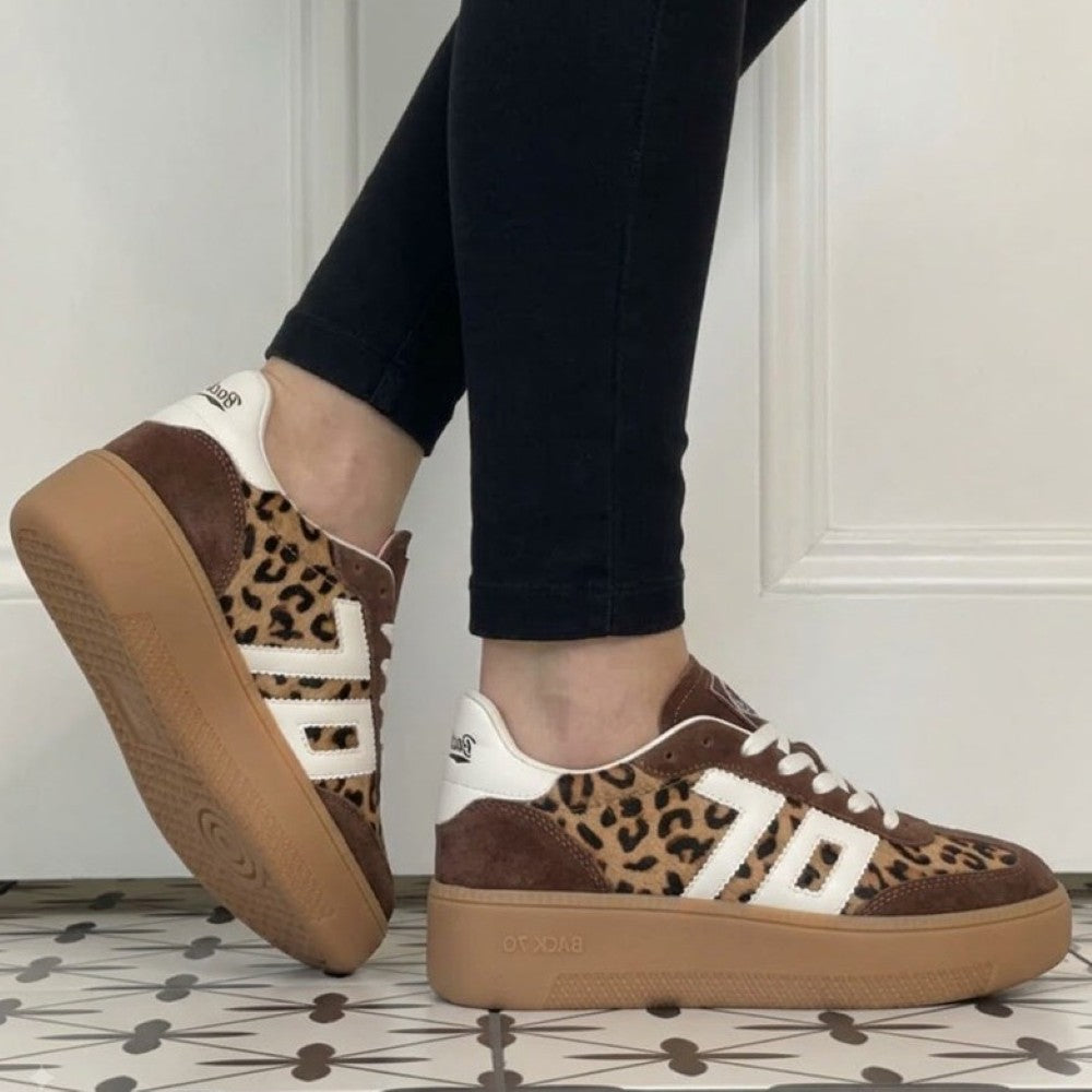 A person wearing Back70 brown suede and leopard-print platform sneakers with white side stripes, paired with black pants, standing on a patterned tile floor.
