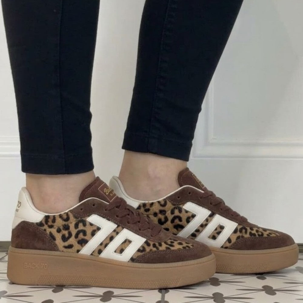 A person wearing Back70 brown suede and leopard-print platform sneakers with white side stripes, paired with black pants, standing on a patterned tile floor.