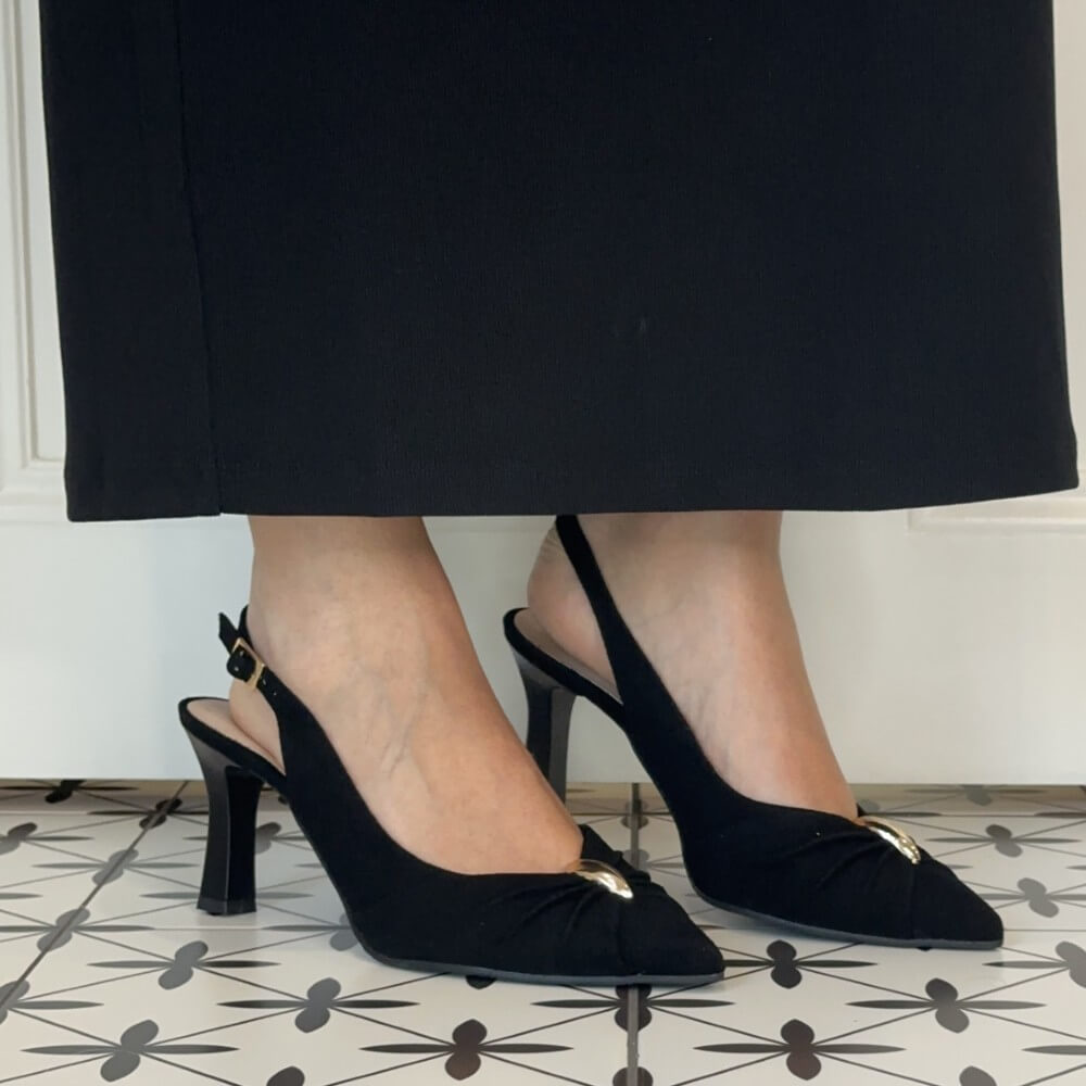 Bioeco Black slingback kitten heel pumps with gold hardware, shown on a model wearing a black skirt over a patterned tile floor.
