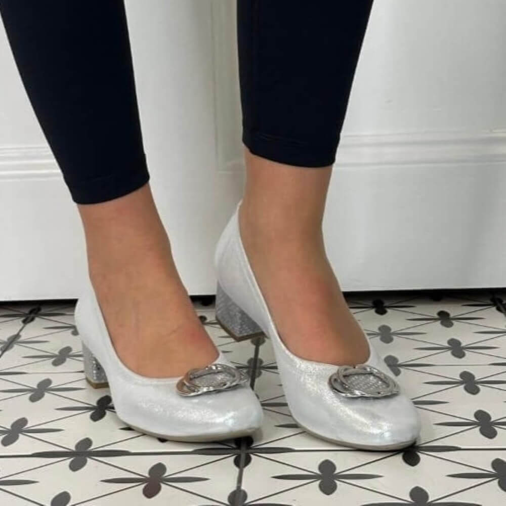 silver glittery shoes with decorative buckles worn by a person on a patterned floor.