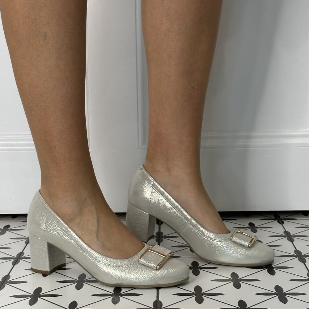 gold high-heeled shoes with a buckle on a patterned floor.