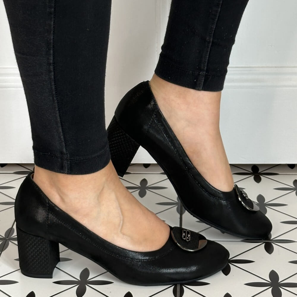 Black high-heeled shoes worn with black pants on a patterned floor. Bioeco 6844 Block Heel Black Shimmer Suede court shoes