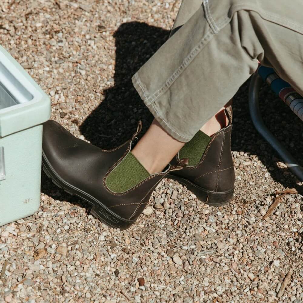 Brown shoes with green accents worn by a person on a gravel surface
