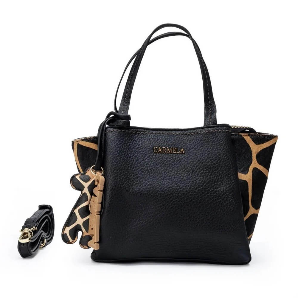 A black pebbled Faux leather handbag with gold-tone hardware and a gold 'CARMELA' logo on the front. The sides of the bag feature a black and tan giraffe print pattern, and a matching detachable shoulder strap with a giraffe charm is displayed to the left on a clean white background.