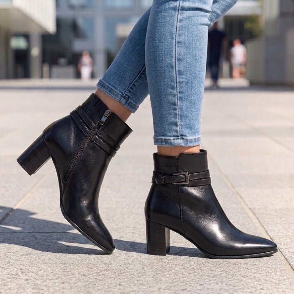 Caprice Black leather ankle boots with block heels and side zippers, shown on a model wearing blue jeans in an outdoor urban setting.