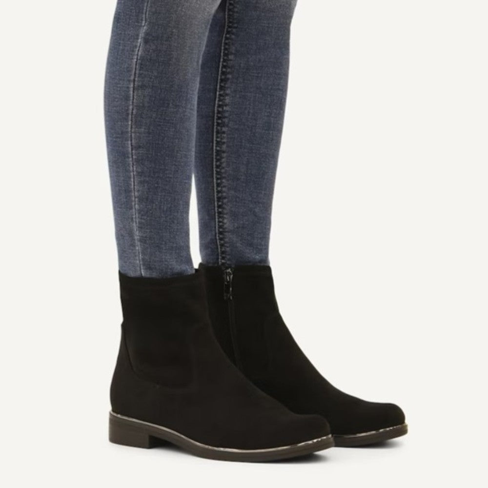 A person wearing Caprice Black Low flat ankle boot and blue jeans on a white background