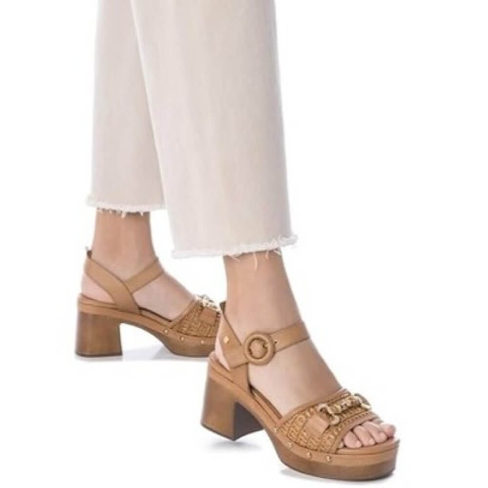 Carmela Tan platform sandals worn with white pants on a white background