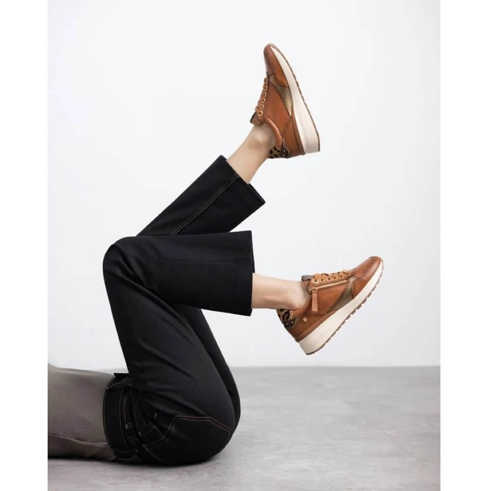 A person reclining on a light gravy floor wearing black cropped pants and Carmela tan leather platform sneakers with brown laces and white soles.