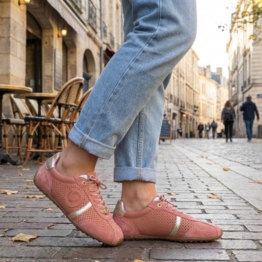 Person wearing pink carmela sneakers with gold accents on a city street.