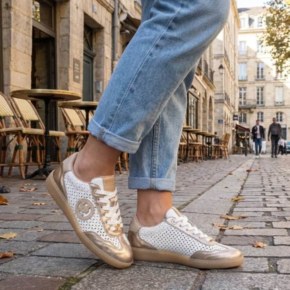 Person wearing white Carmela sneakers with gold accents on a city street.