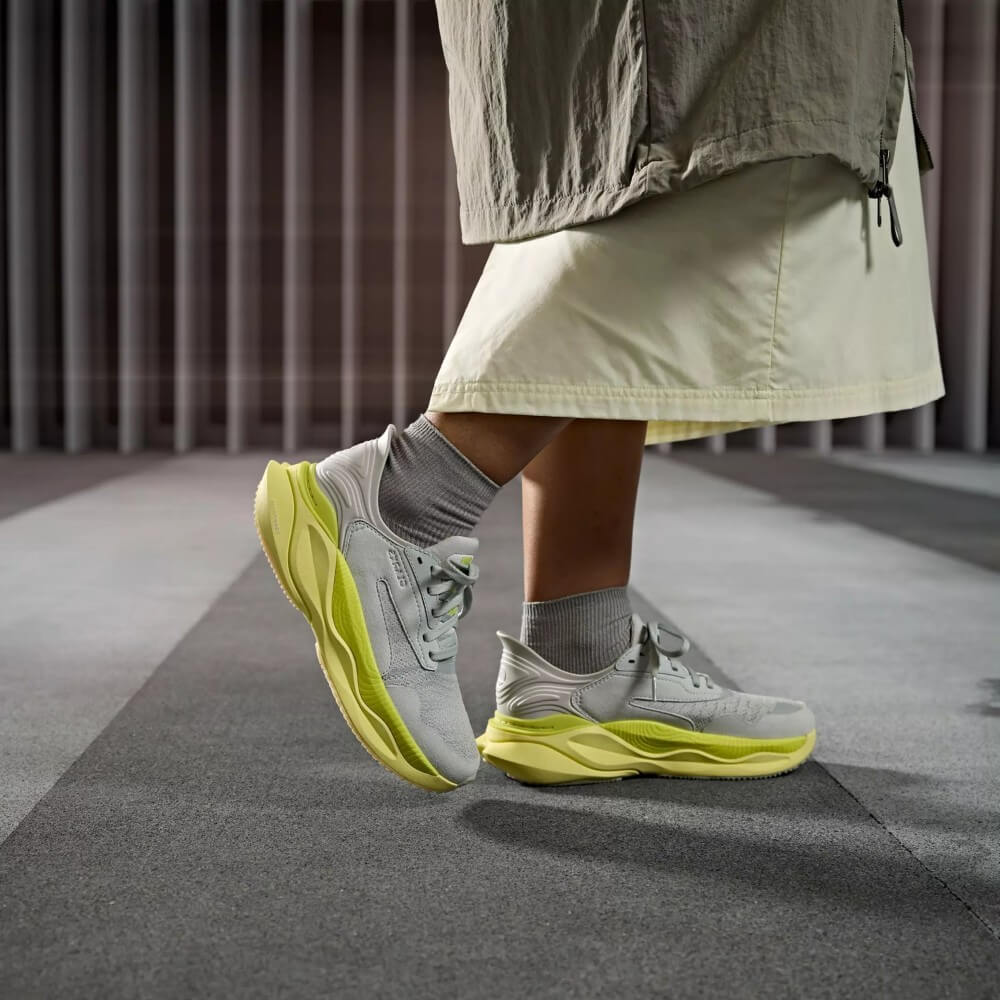 Person wearing Clarks grey sneakers with bright yellow soles on a neutral background