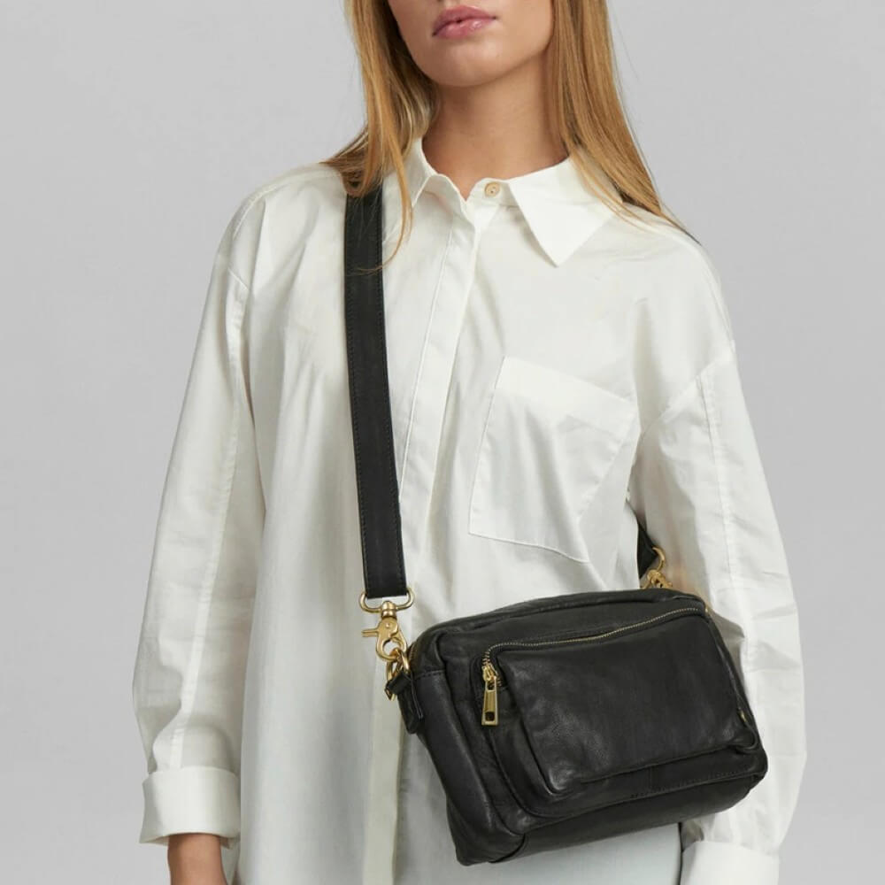 Person wearing a Depeche black leather crossbody bag with a plain background