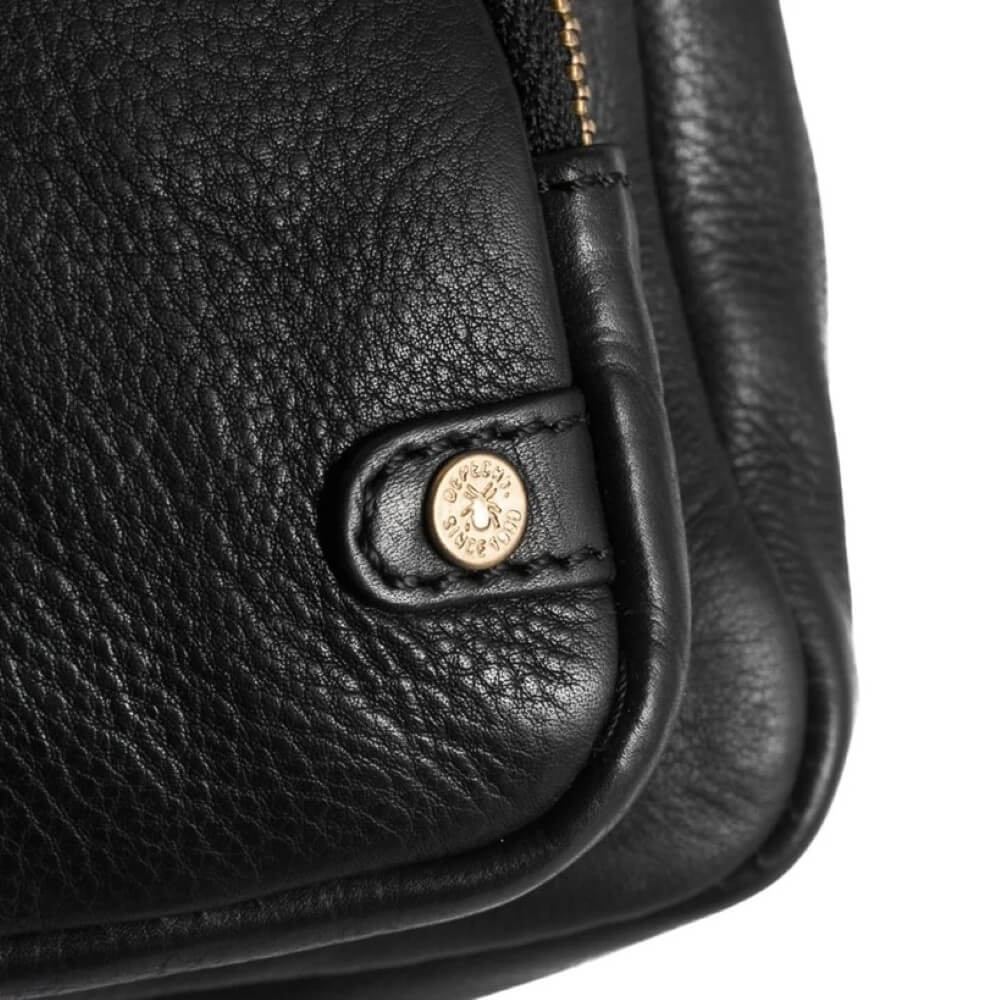 Close-up of a black leather bag with a gold logo on a white background
