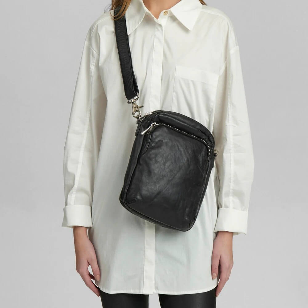 Person wearing a Depeche Black leather crossbody bag with a white shirt
