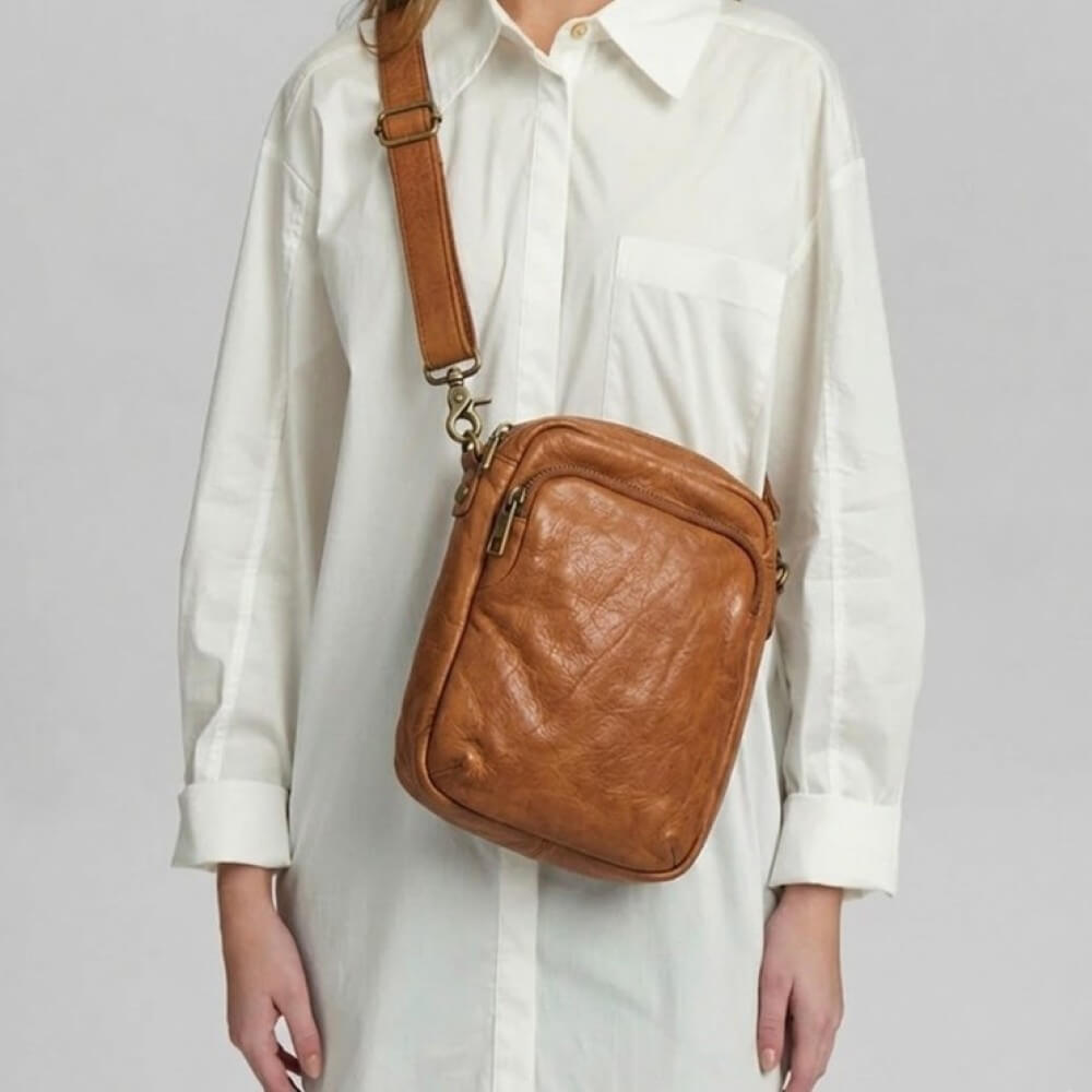 Person wearing a depeche brown leather crossbody bag on a plain background