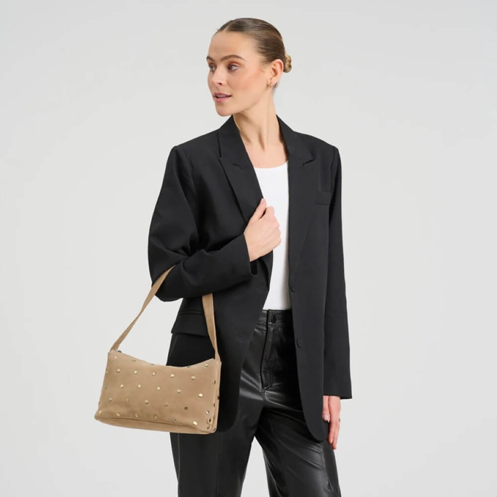Woman wearing a black blazer and holding a Depeche beige handbag on a light grey background