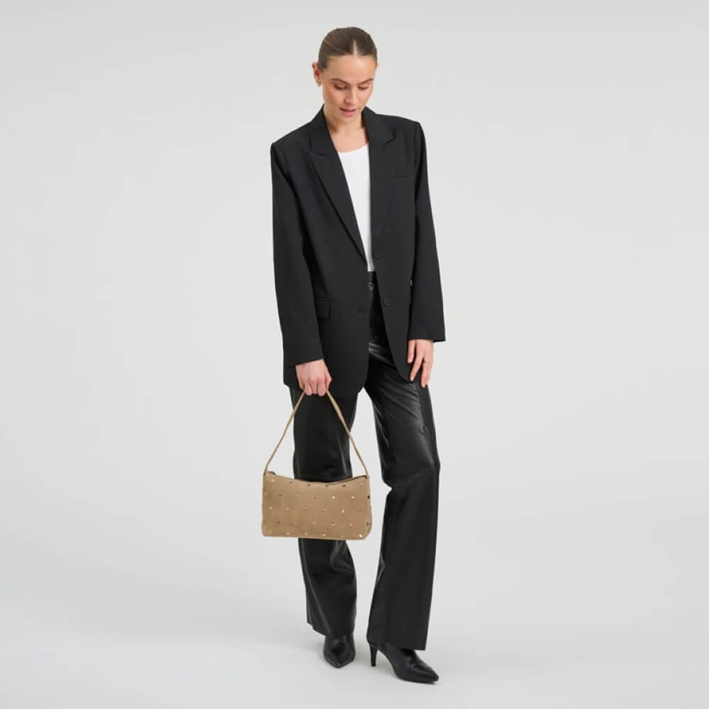 Woman wearing a black blazer and holding a Depeche beige handbag on a light grey background
