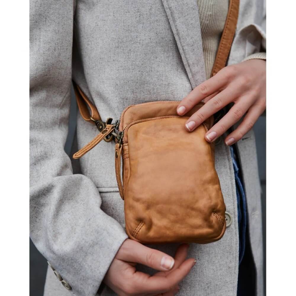 Person holding a Depeche brown leather crossbody bag with a neutral background