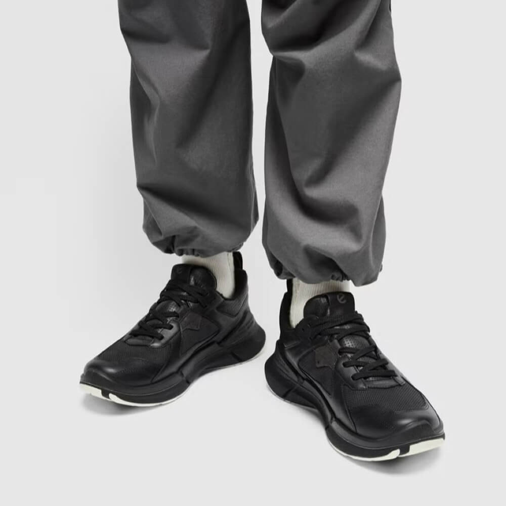 Black sneakers worn with gray pants on a light gray background