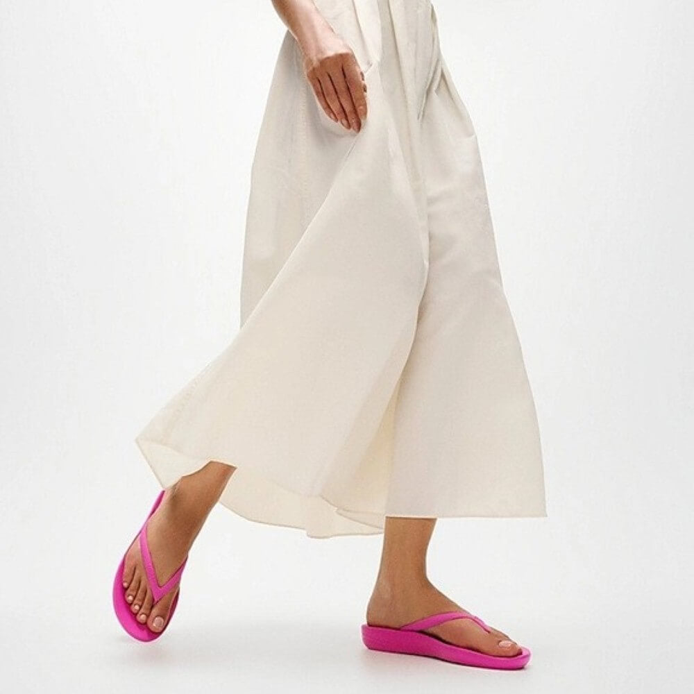 Person wearing bright pink sandals with wide-leg white pants on a light background