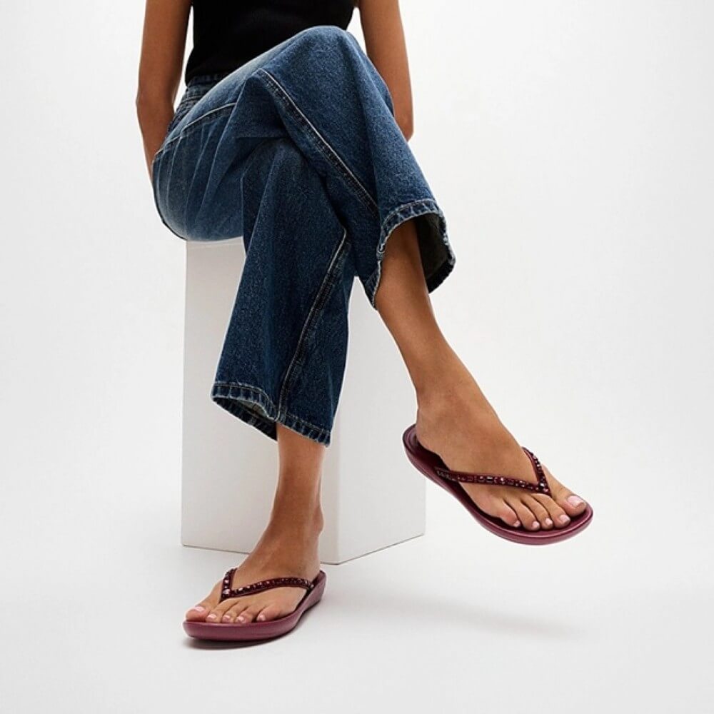 Person wearing blue jeans and wine Fitflop sandals on a white background