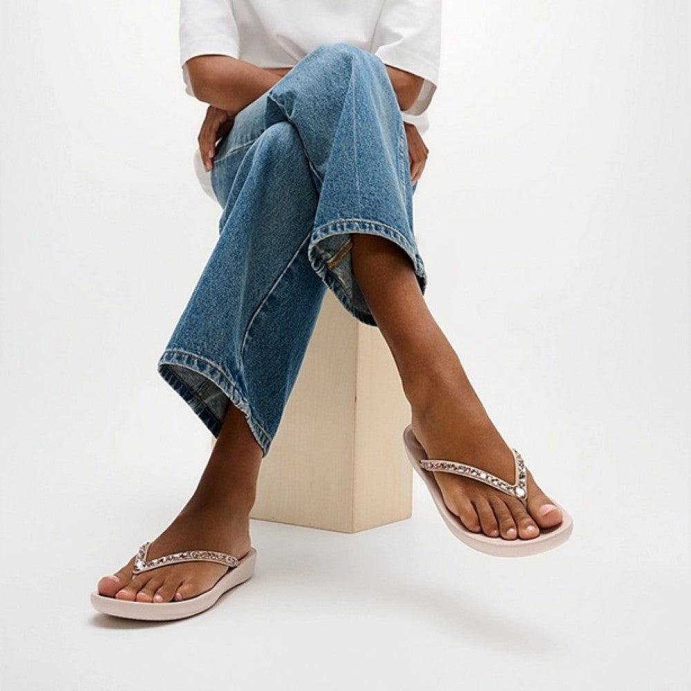 Person wearing light pink sandals with decorative straps on a white background