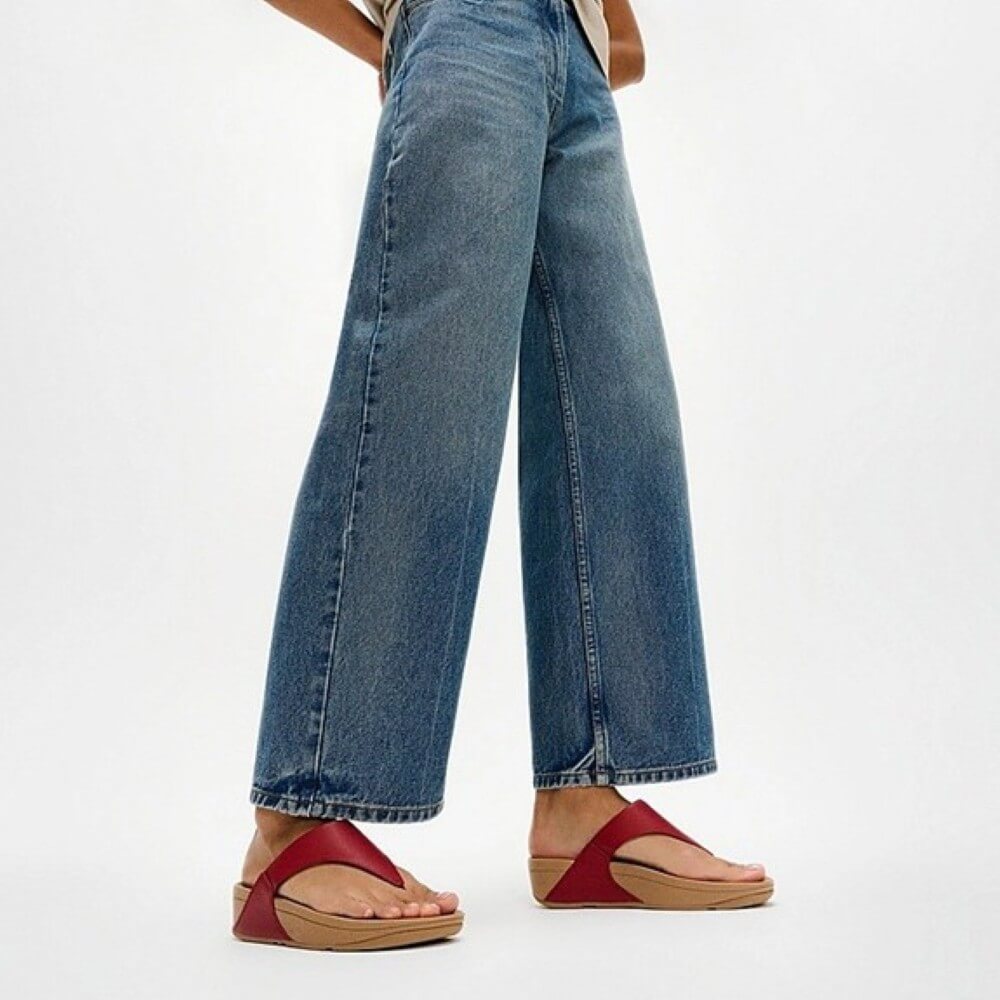 Person wearing blue jeans and red sandals on a white background