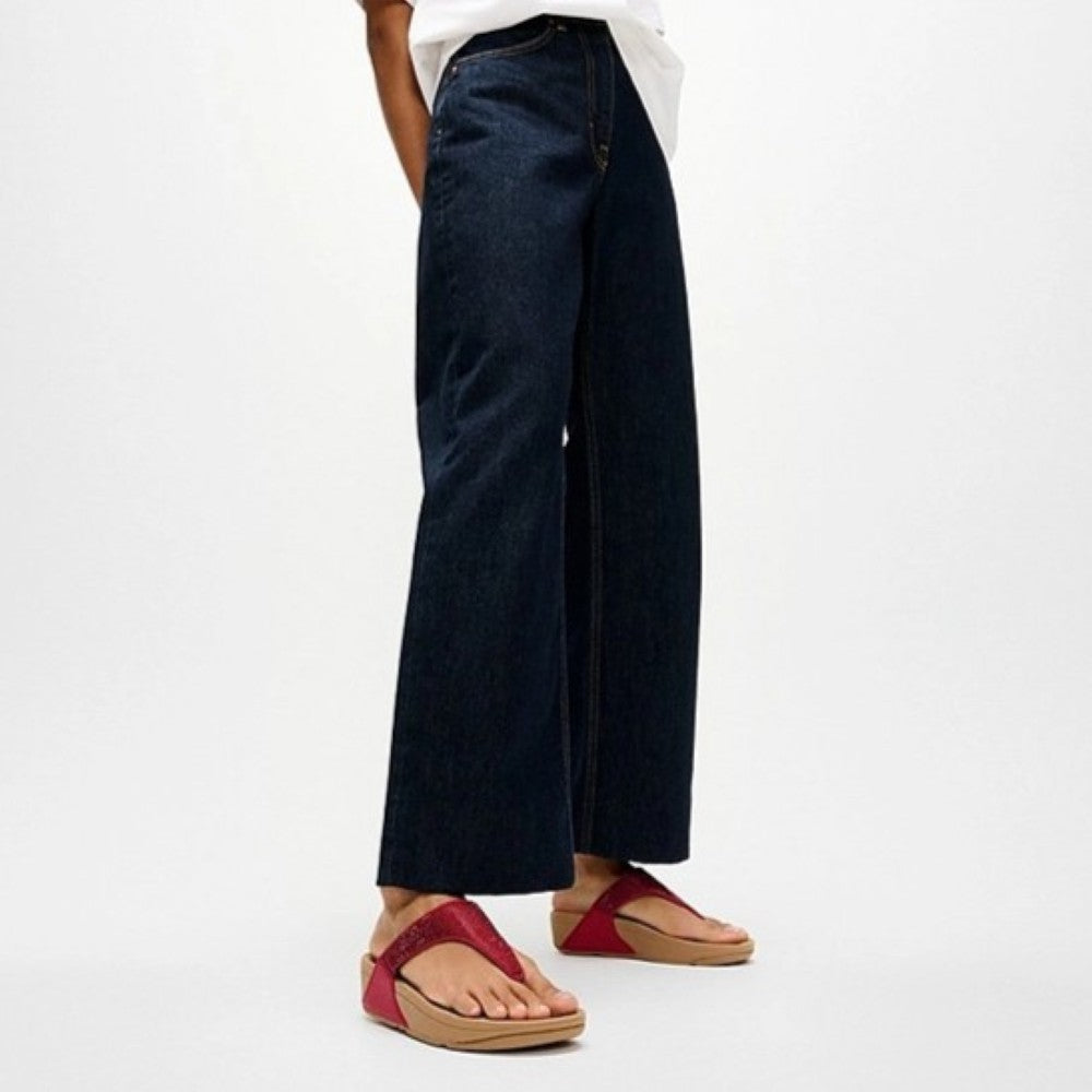Person wearing dark blue wide-leg jeans and red sandals on a white background