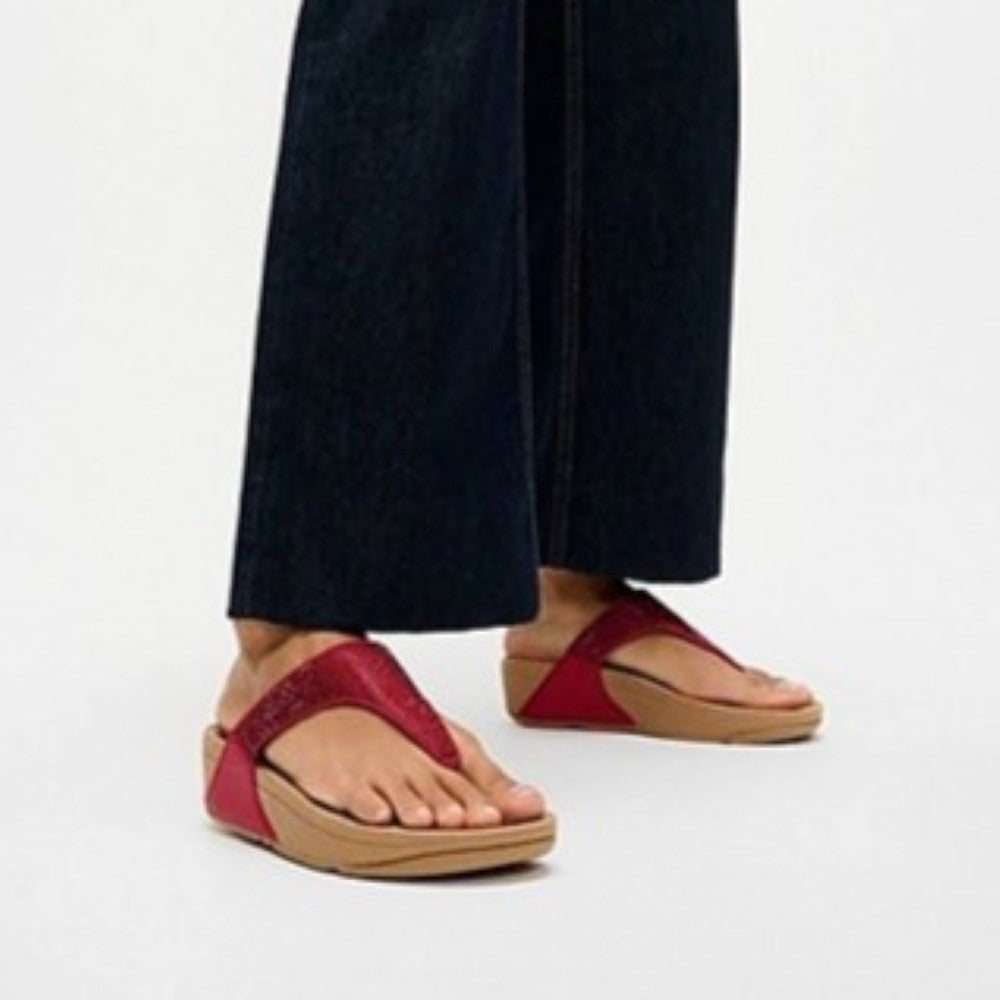 Fitflop Red sandals worn with dark pants on a light background