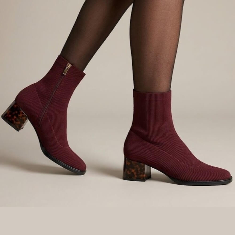 A pair of Gioseppo burgundy ribbed knit ankle boots with tortoiseshell block heels, shown on a model wearing black tights against a light beige studio background.
