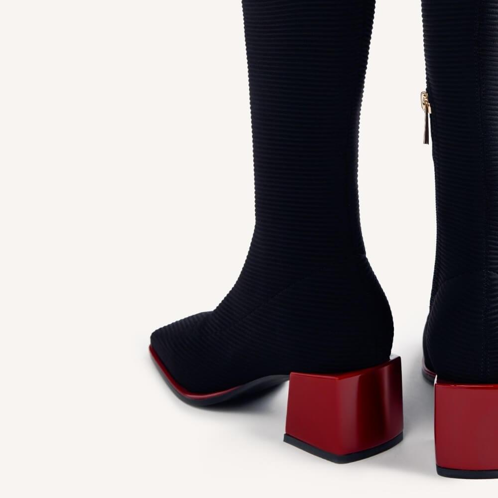 Close-up of a pair of Gioseppo black ribbed knee-high boots with chunky glossy red block heels, shown from the back on a light gray studio background.